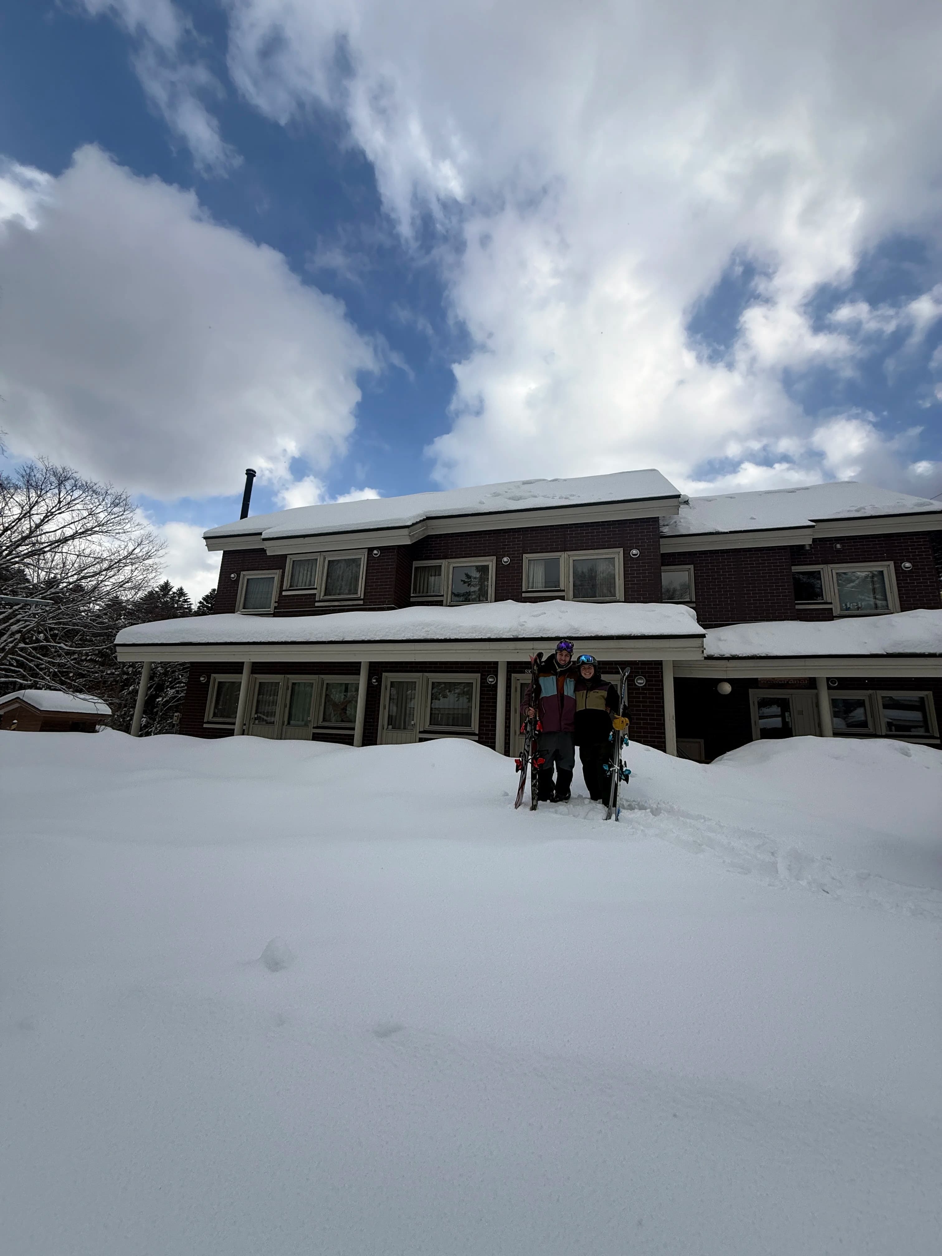 Riley and Denise standing in front of Wakaranai Lodge in winter with skis