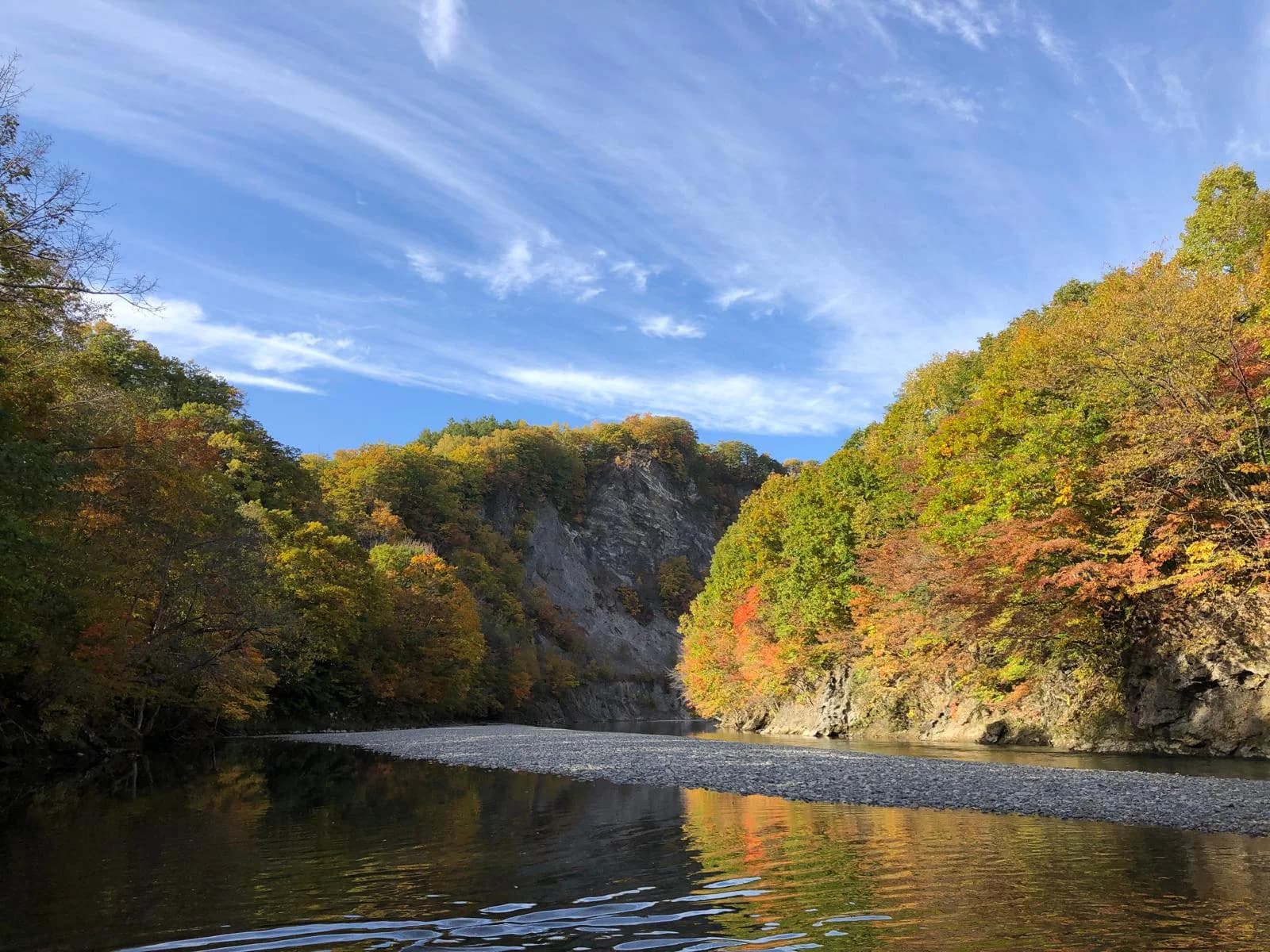 A serene autumn river valley in Hokkaido with colorful foliage, calm water, and clear blue sky